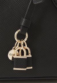 Borsa nera con texture, dotata di minuteria dorata, due accessori a forma di lucchetto e un charm circolare con il marchio attaccato a una tracolla.