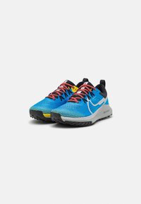 Scarpe da corsa in rete blu con superficie testurizzata, lacci rossi, accenti gialli e supporto al tallone nero. Presentano una intersuola grigia e battistrada robusto.
