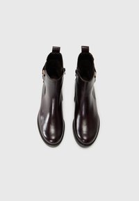 Bottines en cuir bordeaux avec une finition lisse, des fermetures éclair sur les côtés et une semelle en caoutchouc noir épaisse. Présente un design minimaliste et des poignées de tirage.