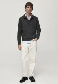 Pullover lavorato a maglia grigio scuro con colletto e patta con tre bottoni, abbinato a pantaloni avorio e scarpe nere stringate. Texture liscia, di media consistenza.