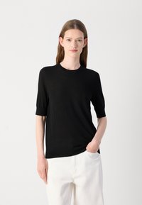 Svart kortermet strikket topp med rund hals. Myk tekstur, tettsittende silhuett og ribbestrikkede mansjetter. Brukt sammen med lyse bukser.