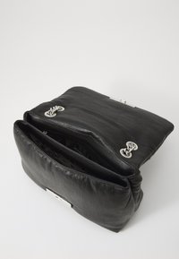 Black leather handbag with silver hardware. Soft texture, rectangular shape, and dual compartments inside. Closure features decorative chains.
