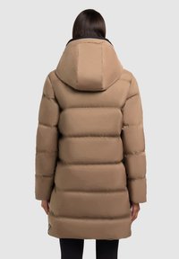 Abrigo acolchado beige con capucha, que presenta un diseño acolchado, mangas largas y una textura suave. La vista trasera muestra una cintura ligeramente entallada.