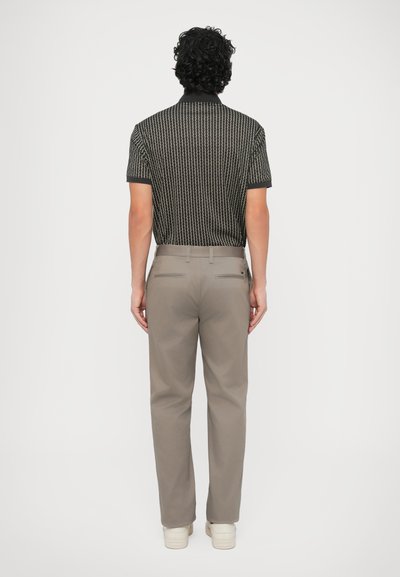 Πόλο μπλουζάκι με κοντά μανίκια, μαύρο με σχέδια, σε συνδυασμό με ανοιχτό γκρι παντελόνι. Το μπλουζάκι διαθέτει γιακά και υφή σχεδίου, ενώ το παντελόνι έχει πίσω τσέπες.