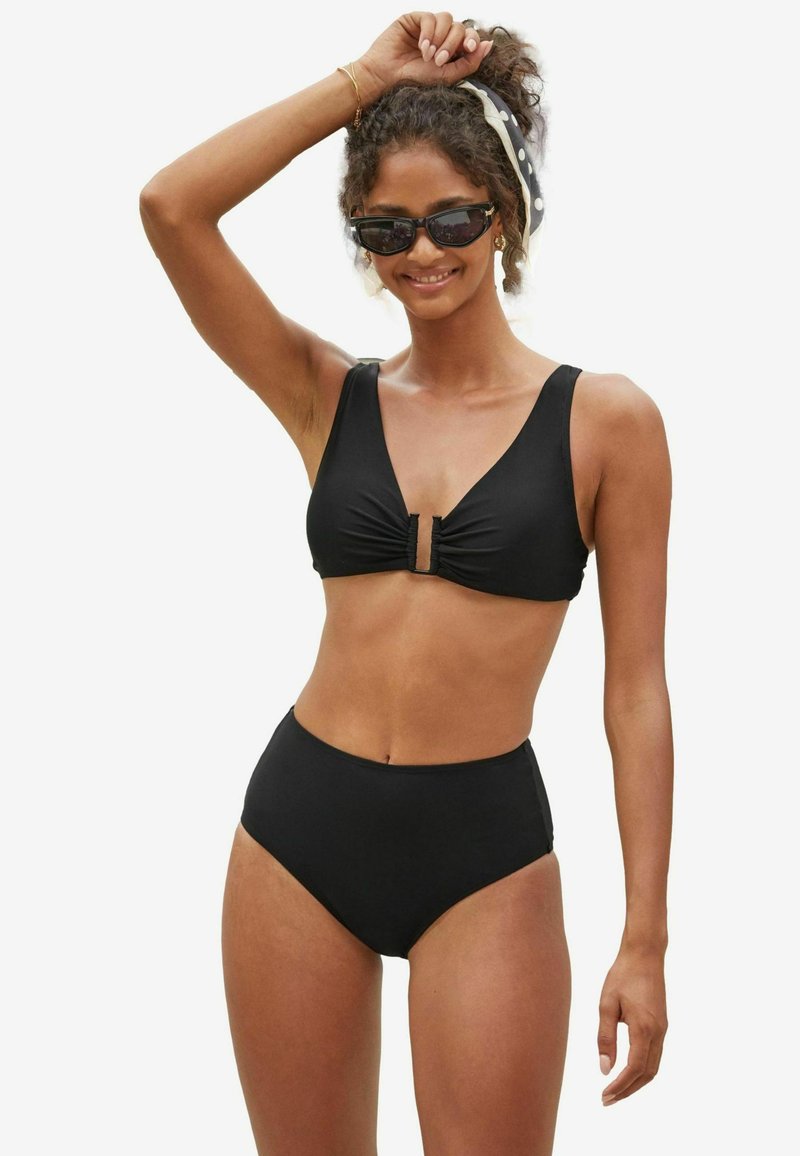 Fekete bikini szett, amely rücskös felsőrésszel rendelkezik, elöl záródik, széles pántokkal és magas derekú alsó résszel, mindez sima, rugalmas anyagból készült.
