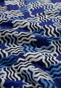 Mėlyna audinio medžiaga su banguotais raštais: tamsiai mėlyna, šviesiai mėlyna ir balta. Medžiaga atrodo tekstūruota ir šiek tiek laisva.