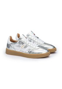 Sneakers metallici argento con accenti bianchi, texture perforata e suole in gomma beige. Presentano lacci e dettaglio del logo sul lato.