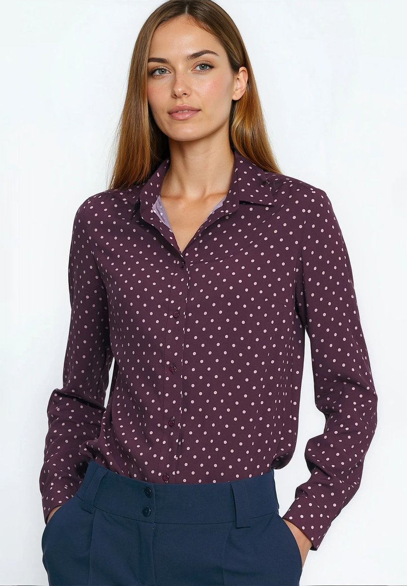 Koszula na guziki w kolorze bordowym z białymi groszkami, z klasycznym kołnierzem i długimi rękawami, zestawiona z granatowymi, wysokim stanem spodniami.