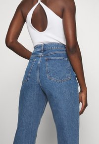 Top blanco de cuello halter con abertura en la espalda, combinado con jeans de mezclilla azul de tiro alto, pierna recta y dos bolsillos traseros.