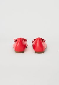 Punaiset nahka-ballet-tossut, joissa on sileä pinta, pyöreä muoto ja koristeellinen nauha takana. Litteä pohja ruskealla värillä.