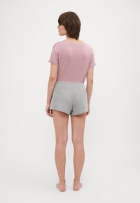 Chemise rose à manches courtes associée à un short gris. La chemise a une coupe décontractée, tandis que le short présente un motif texturé.