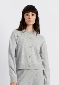 Cardigan grigio a maglia con maniche lunghe, scollatura rotonda e chiusura a cinque bottoni. Orlo e polsini a coste. Trama morbida.