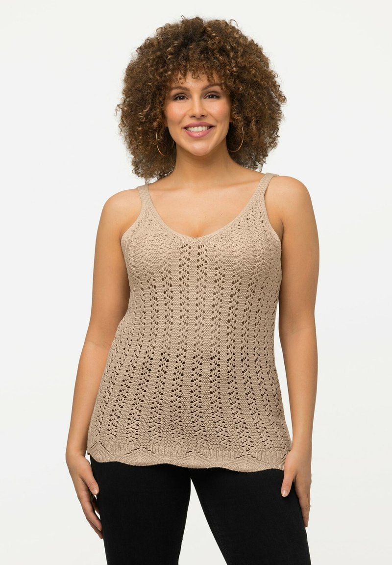 Top a canotta lavorato a maglia beige con scollo a V e spalline larghe, caratterizzato da un motivo testurizzato e orlo a scallop. Abbinato a un pantalone nero.
