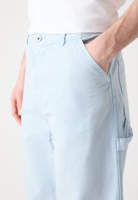 Lys blå bomullsbukser med en avslappet passform, med frontlommer og en enkelt sidelomme. Stoffet har en jevn tekstur.