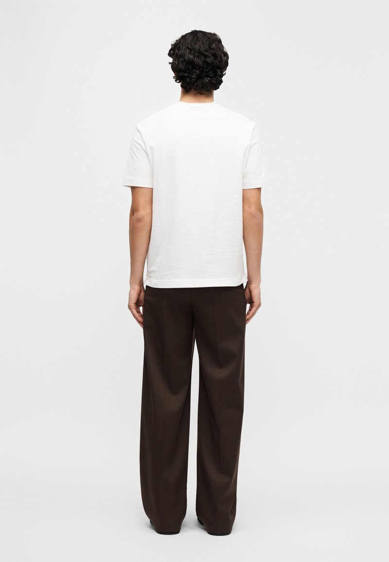 White cotton t-shirt with short sleeves, back view, paired with brown wide-leg trousers, plain design, smooth texture.