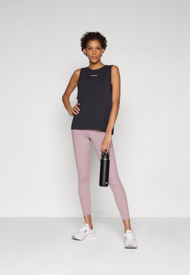 Haut sans manches noir, leggings roses et chaussures de sport blanches. Le modèle tient une bouteille d'eau noire. Tissu lisse, design ajusté, détails de logo minimaux.