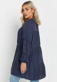 Navy blue long-sleeve top with a relaxed fit, pleated design, and elasticized cuffs. Lightweight fabric with a textured finish.