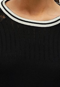 Czarny sweter z pionowym prążkowaniem, z dekoltem w srebrno-czarne paski. Materiał wydaje się miękki z teksturowanym wykończeniem.