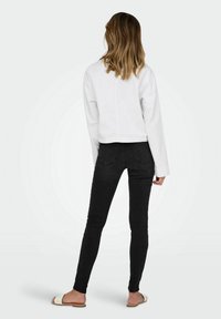 Sweatshirt blanc court à manches longues associé à un jean skinny noir et des sandales plates de couleur claire, vu de dos.