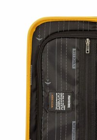 Interno in tessuto nero di una valigia con zip gialla; presenta stampe di modelli di volo e un'etichetta nera con testo bianco.