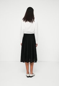 Fustă neagră plisată, cu talie ajustată, asortată cu o bluză albă cu mâneci lungi. Fusta ajunge sub genunchi și are o textură fluidă.