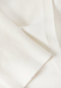 Tissu tricoté blanc avec une texture lisse, plié pour montrer un design en V et des coutures visibles le long des bords.