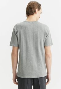 Szary sweter z krótkim rękawem o pionowej fakturze prążkowanej, z okrągłym dekoltem i lekko luźnym krojem, w połączeniu z ciemnymi, prążkowanymi spodniami.