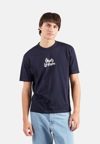 Camiseta de algodón navy de manga corta, con cuello redondo y un gráfico blanco de "Guess Los Angeles" en el pecho. Ajuste básico con dobladillo recto.