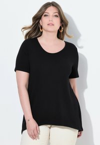 T-shirt nera a maniche corte con scollatura rotonda e una vestibilità comoda, realizzata in stoffa morbida. Il modello è in piedi su uno sfondo chiaro.