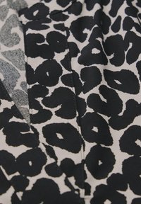 Tessuto con stampa leopardata in bianco e nero con una texture liscia, caratterizzato da grandi forme nere curve su uno sfondo chiaro, con dettagli di cucitura visibili.