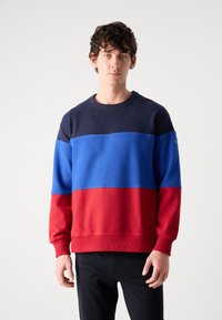 Crewneck sweatshirt featuring navy, blue, and red vertical stripes. Made of soft fabric with ribbed cuffs and hem.
