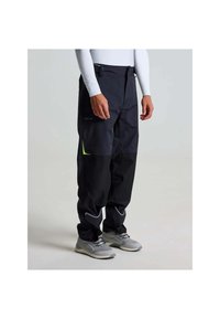 Waterdichte zwarte broek met reflecterende accenten, elastische tailleband en verstelbare boorden, gecombineerd met grijze sportschoenen.