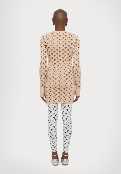 Vestido beige de manga larga con estampado de luna creciente, combinado con leggings blancos que presentan patrones de lunas crecientes en negro. Textura suave, diseño ajustado.