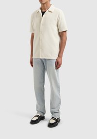 Korte mouw, crèmekleurig gemêleerd shirt met een spread collar, met knoopsluiting, gecombineerd met lichtblauwe jeans en zwarte loafers.