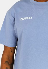 Lichtblauwe katoenen t-shirt met een relaxte pasvorm. Voorzien van een witte "PARADISIO" logo op de borst, korte mouwen en een ronde halslijn.