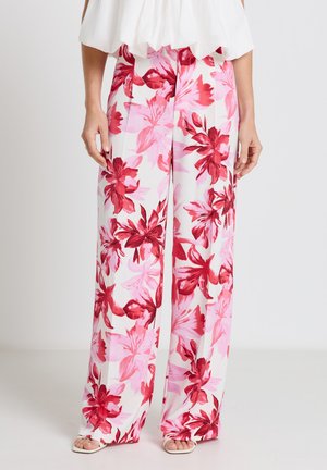 Pantaloni bianchi a gamba larga con grande stampa floreale rosa e rossa, indossati con un top bianco e sandali open toe.