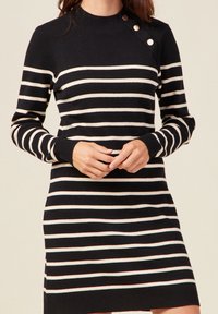 Robe en tricot avec un col haut, fond noir et rayures horizontales crème et rose pâle. Présente trois boutons décoratifs sur l'épaule.