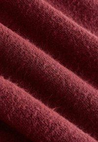 Bordový vlnitý textil s mäkkou, jemnou textúrou a jemnými variáciami v hustote, vykazujúci teplú, bohatú farbu a mierny lesk.