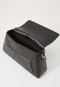 Borsa in pelle nera con una forma strutturata, dotata di chiusura a pattina, due tasche frontali e un accento in metallo circolare argentato.