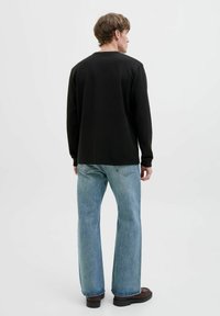 Chemise noire à manches longues avec une finition texturée, associée à un jean droit bleu clair et des bottes foncées. Design minimaliste, sans logos visibles.