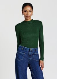 Grünes, geripptes Langarmoberteil mit hohem Kragen, kombiniert mit hoch taillierten blauen Jeans aus Denim mit großen Gesäßtaschen.