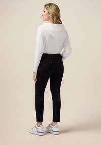 Vit huvtröja med lång ärm, tillsammans med svarta åtsittande byxor och vita sneakers med silverdetaljer. Enkelt och modernt design.