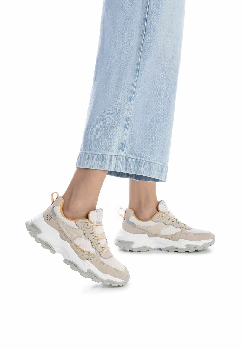 Zapatillas de malla en color beige y blanco con suela de goma gruesa, acentuadas con sutiles detalles en naranja. Presentan una puntera redondeada y diseño de cordones.