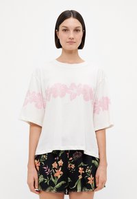Witte t-shirt met korte mouwen en een roze bloemenprint over de borst, gecombineerd met zwarte shorts met een kleurrijk bloemenpatroon en een rafelige zoom.