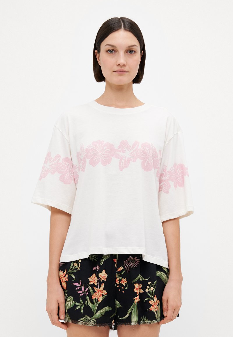 Witte t-shirt met korte mouwen en een roze bloemenprint over de borst, gecombineerd met zwarte shorts met een kleurrijk bloemenpatroon en een rafelige zoom.