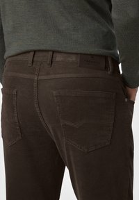 Rückansicht einer Person, die braune Cordhosen mit Gesäßtaschen und einen in die Hose gesteckten grünen Pullover trägt.
