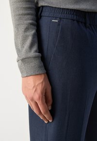 Granatowe spodnie z elastycznym pasem, wykonane z gładkiej tkaniny o subtelnej fakturze. Szara bluzka z długim rękawem z podwiniętymi mankietami.