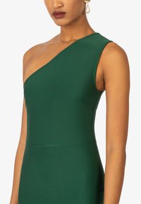 Robe verte à une épaule fabriquée en tissu texturé. Présente une silhouette ajustée et des détails de couture, avec une finition lisse et un léger brillant.