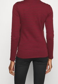 Top de manga larga a rayas rojo y negro con escote redondo y silueta ajustada. Fabricado en una suave tela texturizada con un acabado liso.