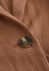 Tissu marron avec un bouton rond brillant cousu dans un boutonnière cousue sur un vêtement plié.